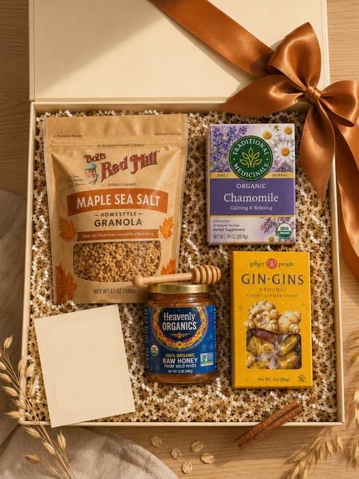 An open cream gift box packed with granola, raw honey, chamomile tea and ginger chews, finished with a copper satin ribbon